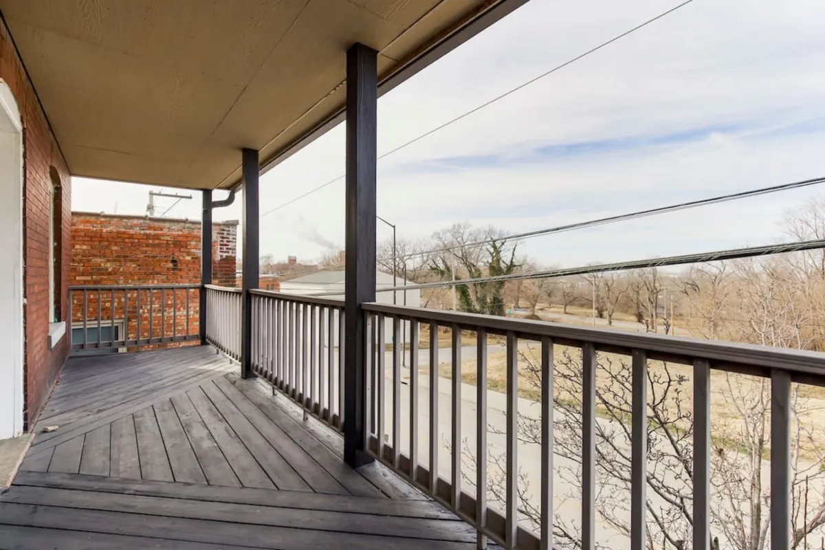 The exterior scene presents a wooden railing and open space with a view of the surrounding natural environment. Soft morning light filters through the trees, creating a peaceful mood for relaxing, socializing, or observing local wildlife.