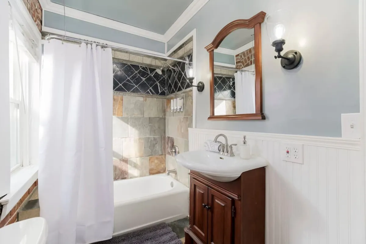 A serene bathroom interior with a bathtub, sink, mirror, and wall tiles, exuding a calming ambiance perfect for unwinding and self-care.
