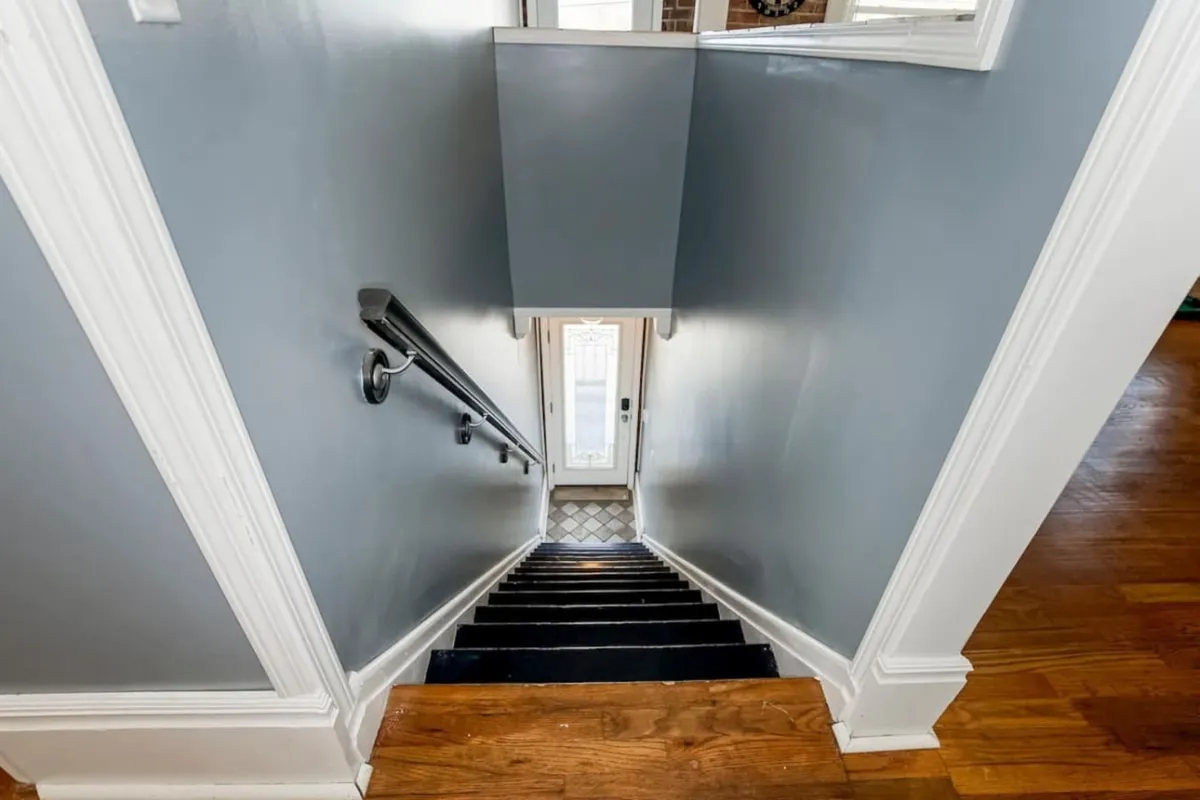 A view of the entryway with a staircase, open doorway, and handrail, radiating warmth and a sense of arrival. The scene suggests coming home and the anticipation of stepping into a welcoming space ready for gatherings.